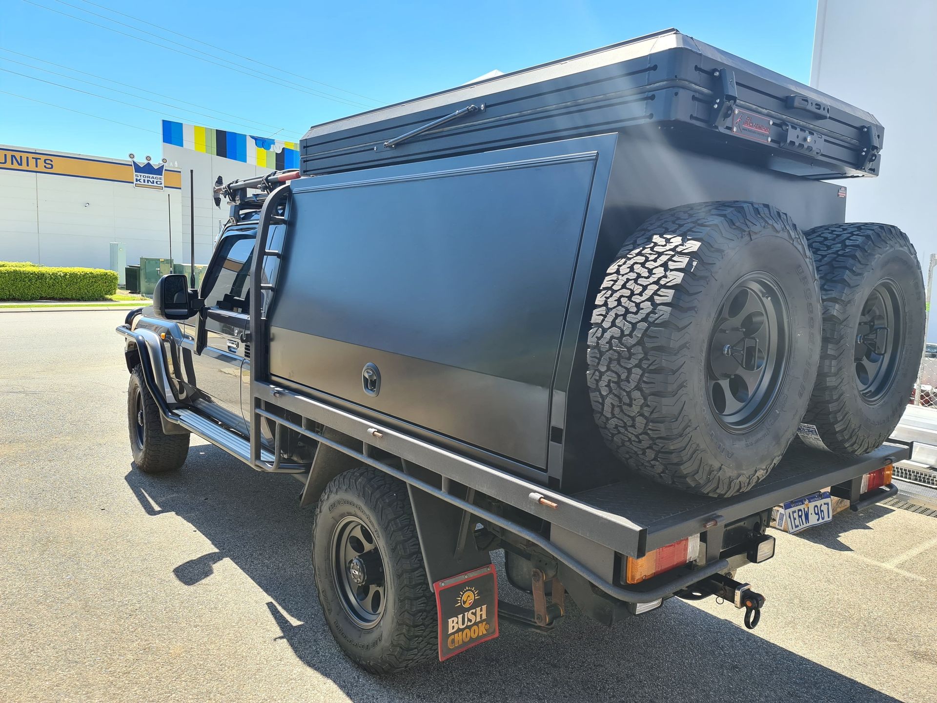 A black truck with a canopy on top of it is parked in a parking lot.
