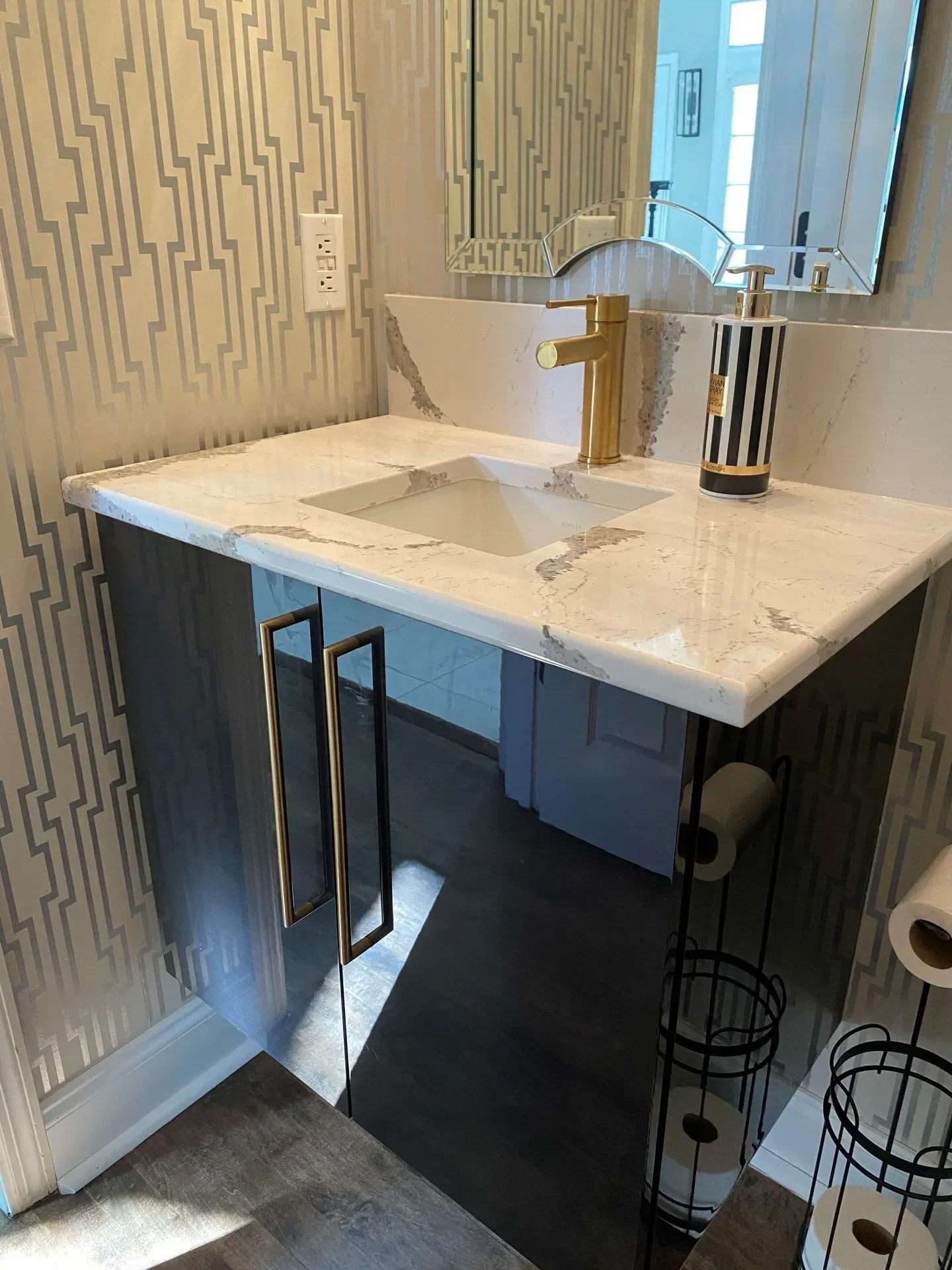 A bathroom with a sink , mirror and toilet paper holder.
