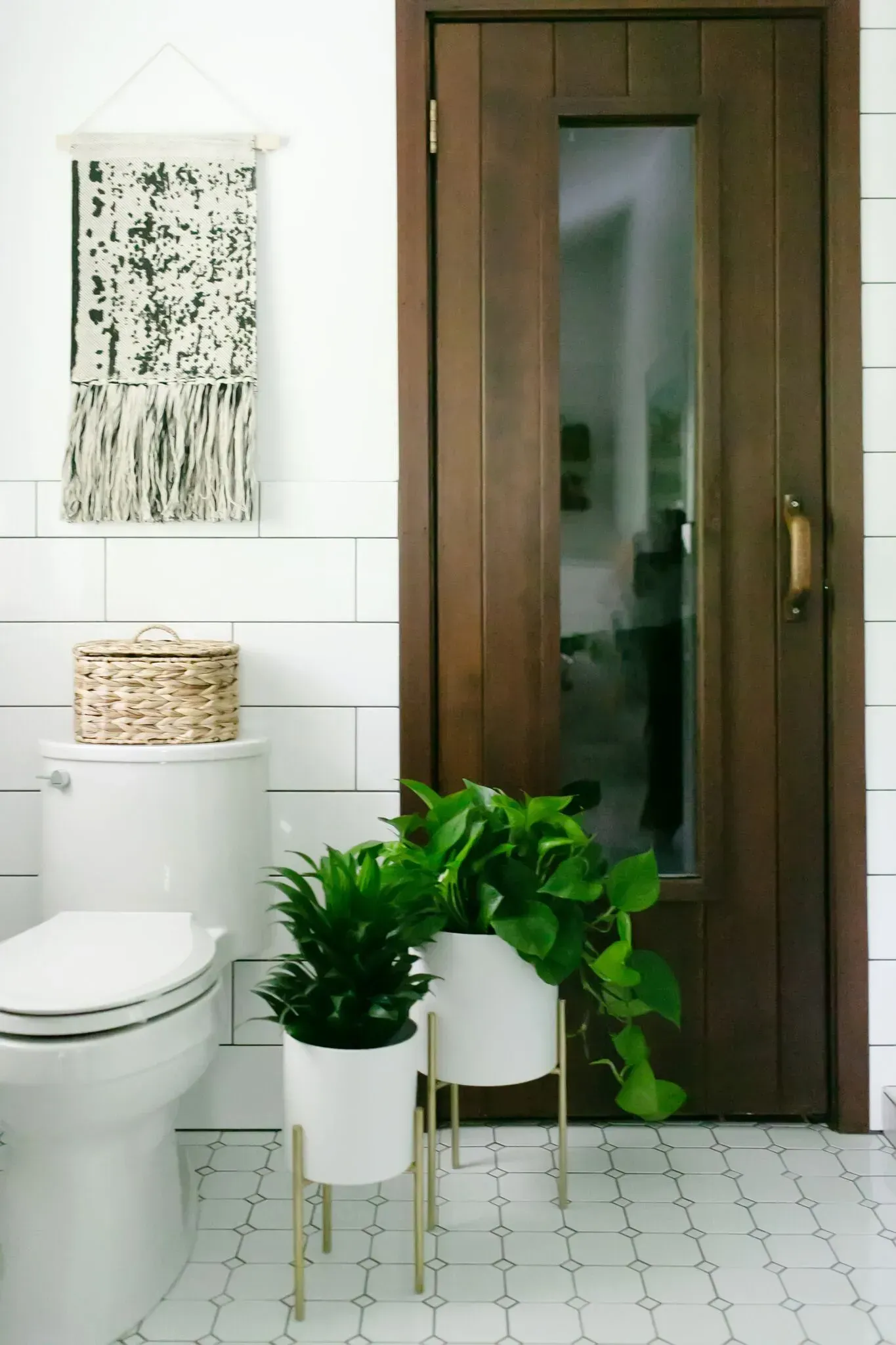 A bathroom with a toilet , potted plants , and a wooden door.