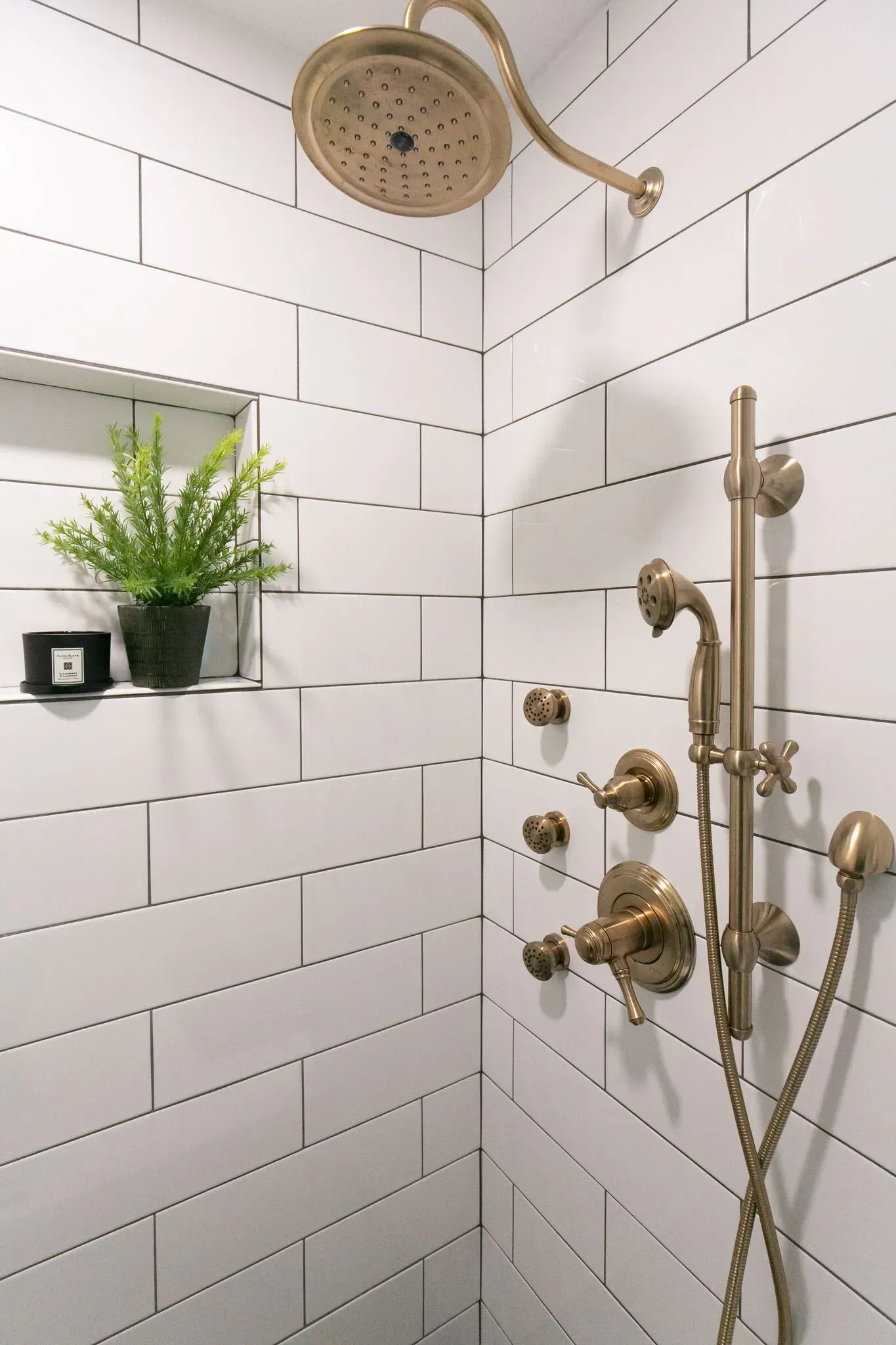A shower with white tiles and gold shower head