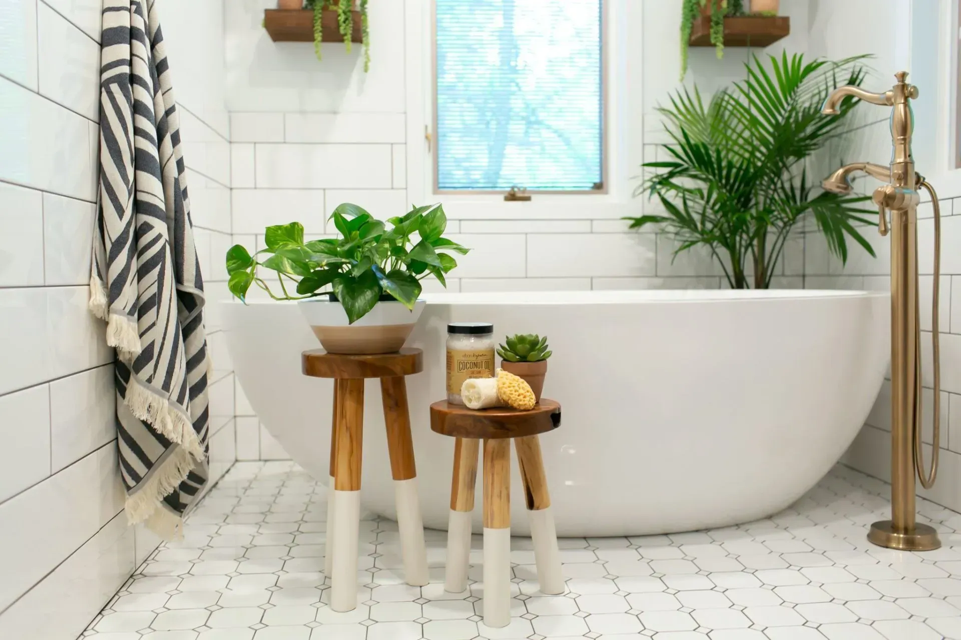 A bathroom with a bathtub , stools , plants and a window.