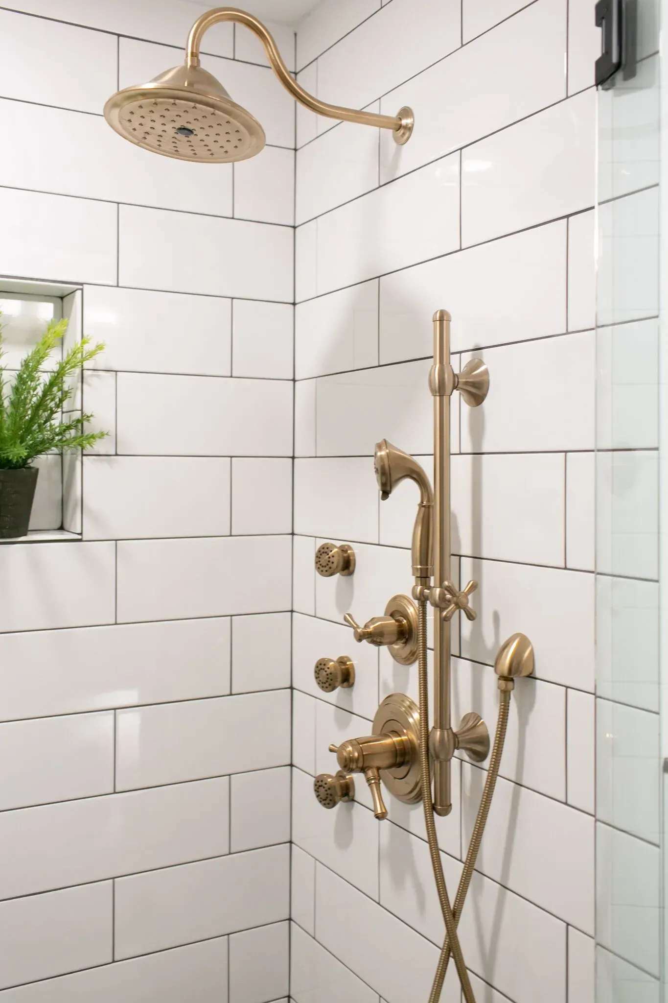 A bathroom with white tiles and a gold shower head.
