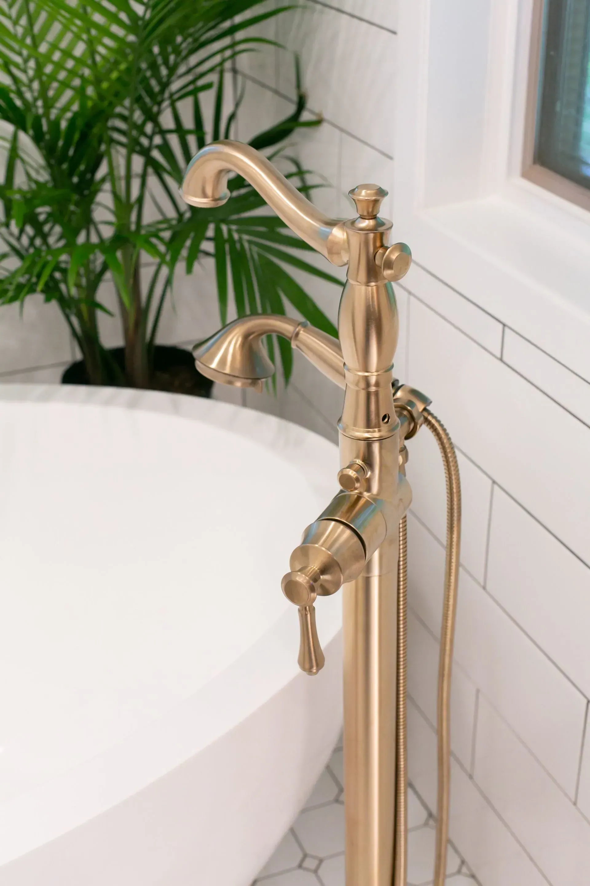 A gold bathtub faucet is next to a white bathtub in a bathroom.