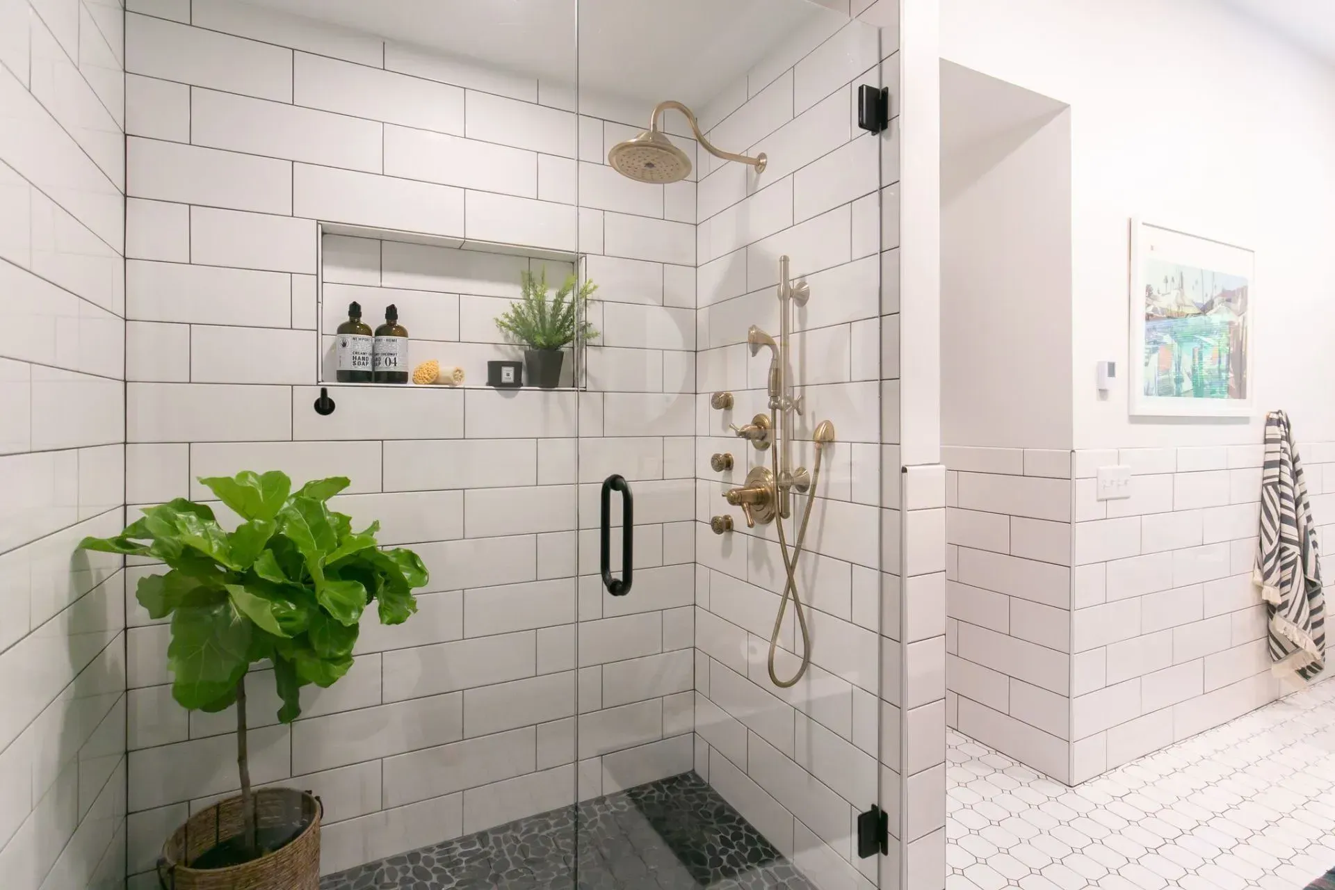 A bathroom with white tiles and a walk in shower with a glass door