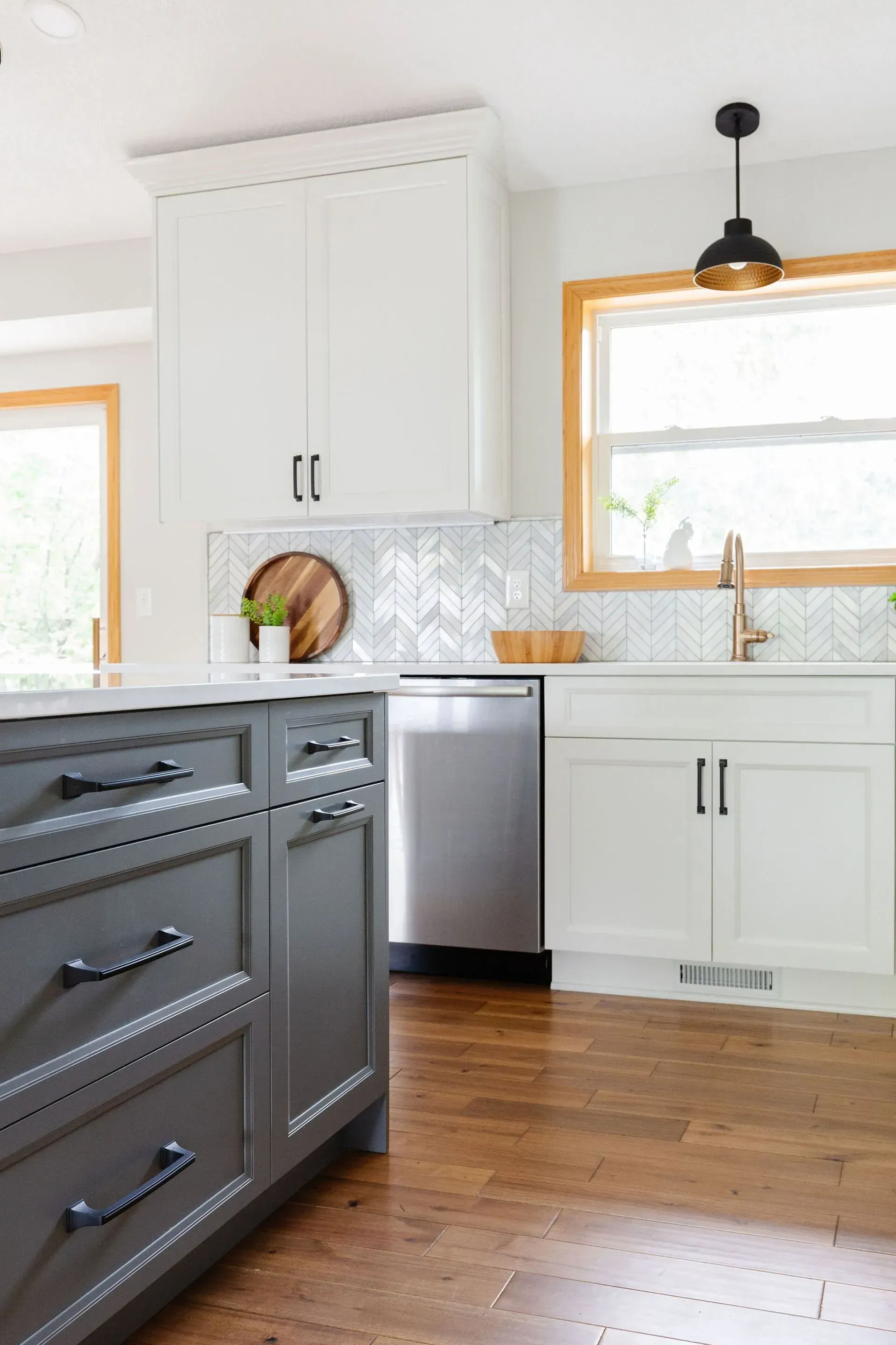 A kitchen with gray cabinets , white cabinets , a stainless steel dishwasher , a sink and a window.