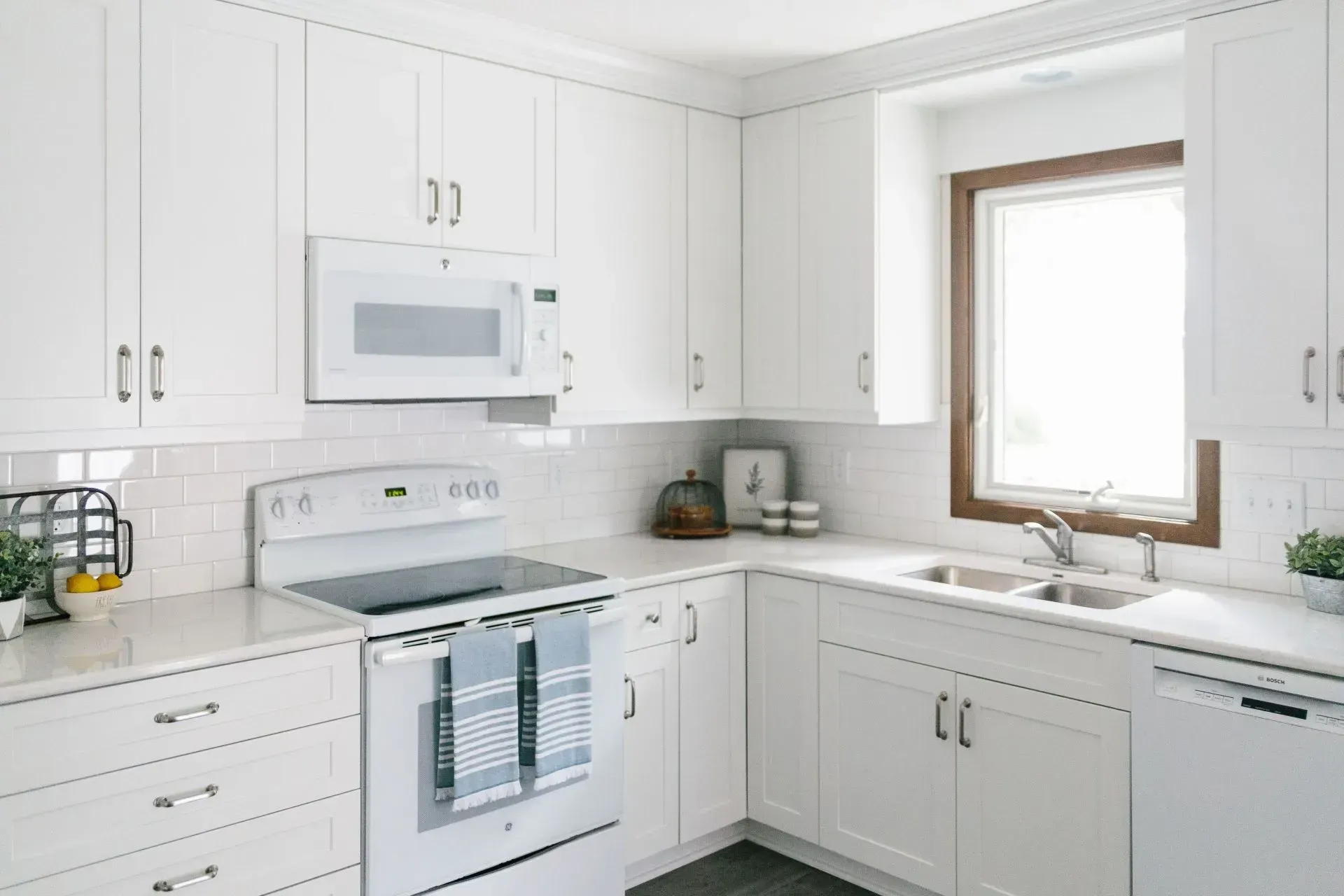 A kitchen with white cabinets , a stove , a sink , and a window.