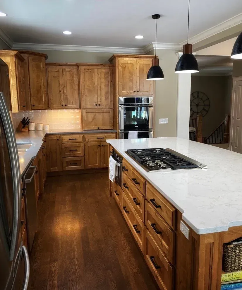 A kitchen with wooden cabinets and a large island with a stove top oven.