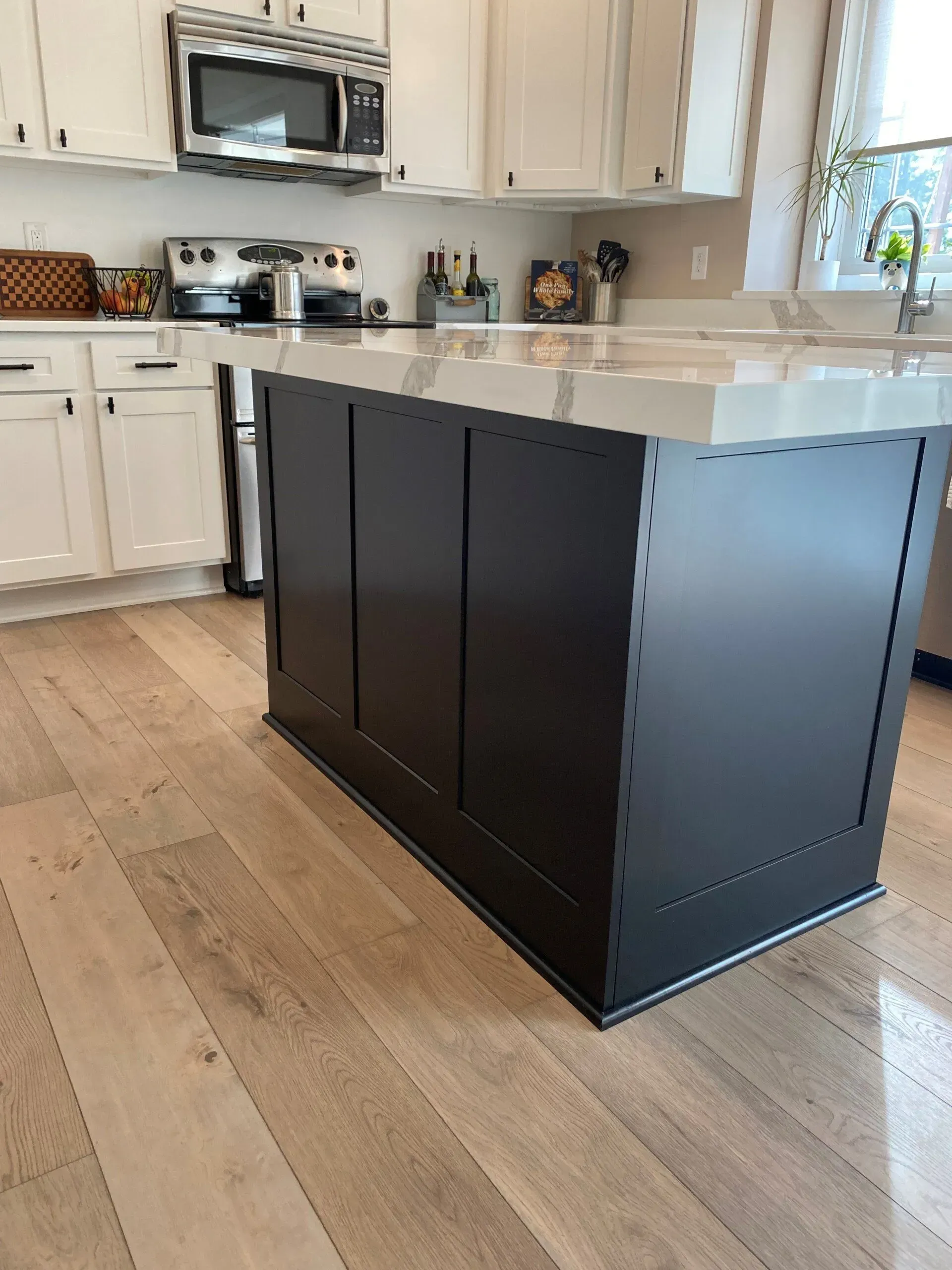 A kitchen with white cabinets and a black island in the middle.