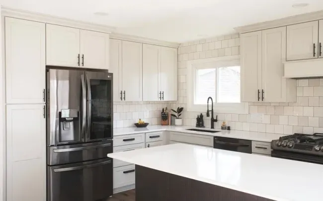 A kitchen with white cabinets , stainless steel appliances , a refrigerator and a sink.