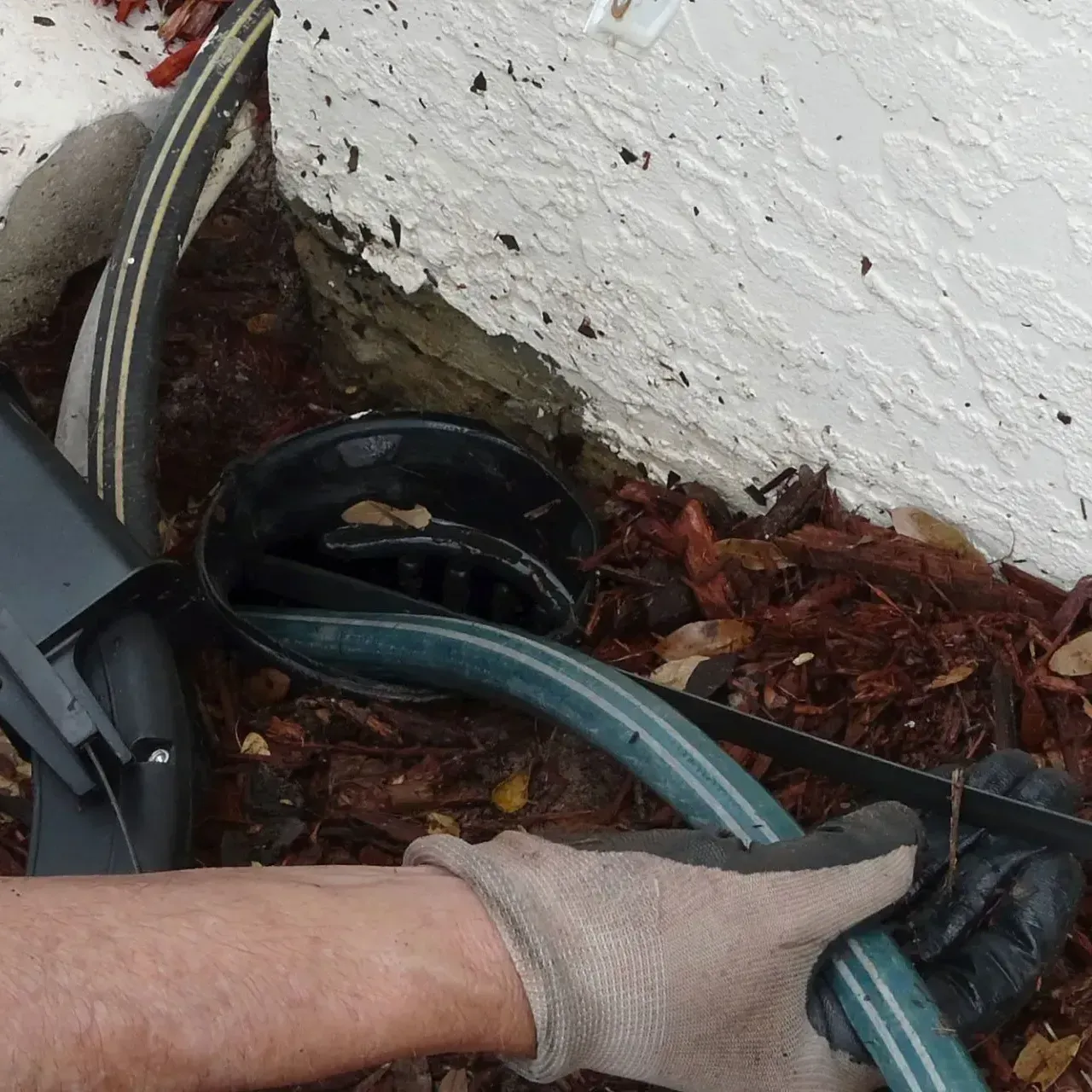 A person wearing gloves is holding a green hose