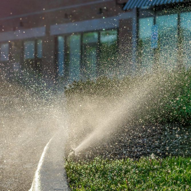 A lawn sprinkler is spraying water on a lush green lawn.