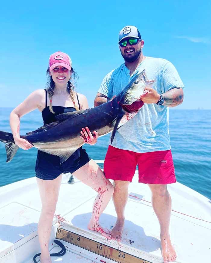 A man and a woman are standing on a boat holding a large fish.