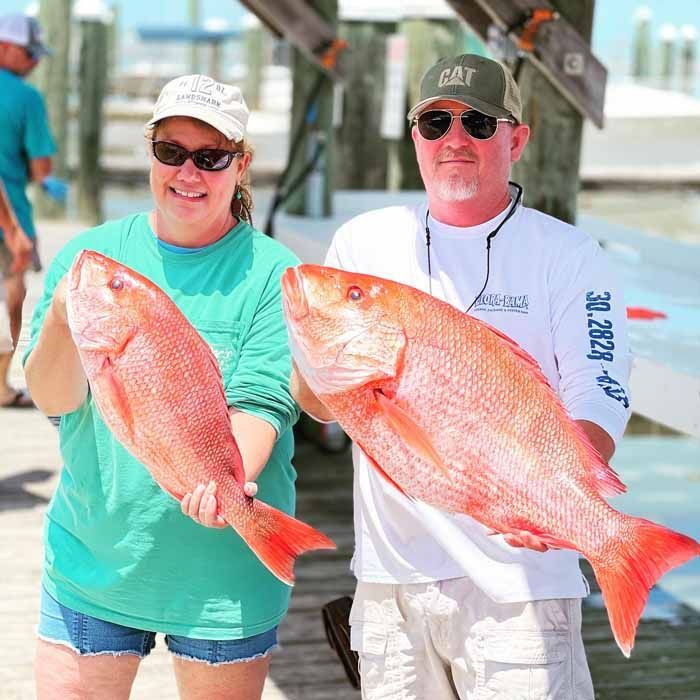 A man and a woman are holding large red fish