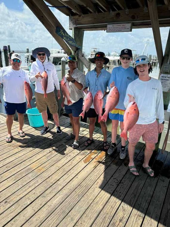 A group of men are standing on a dock holding fish.