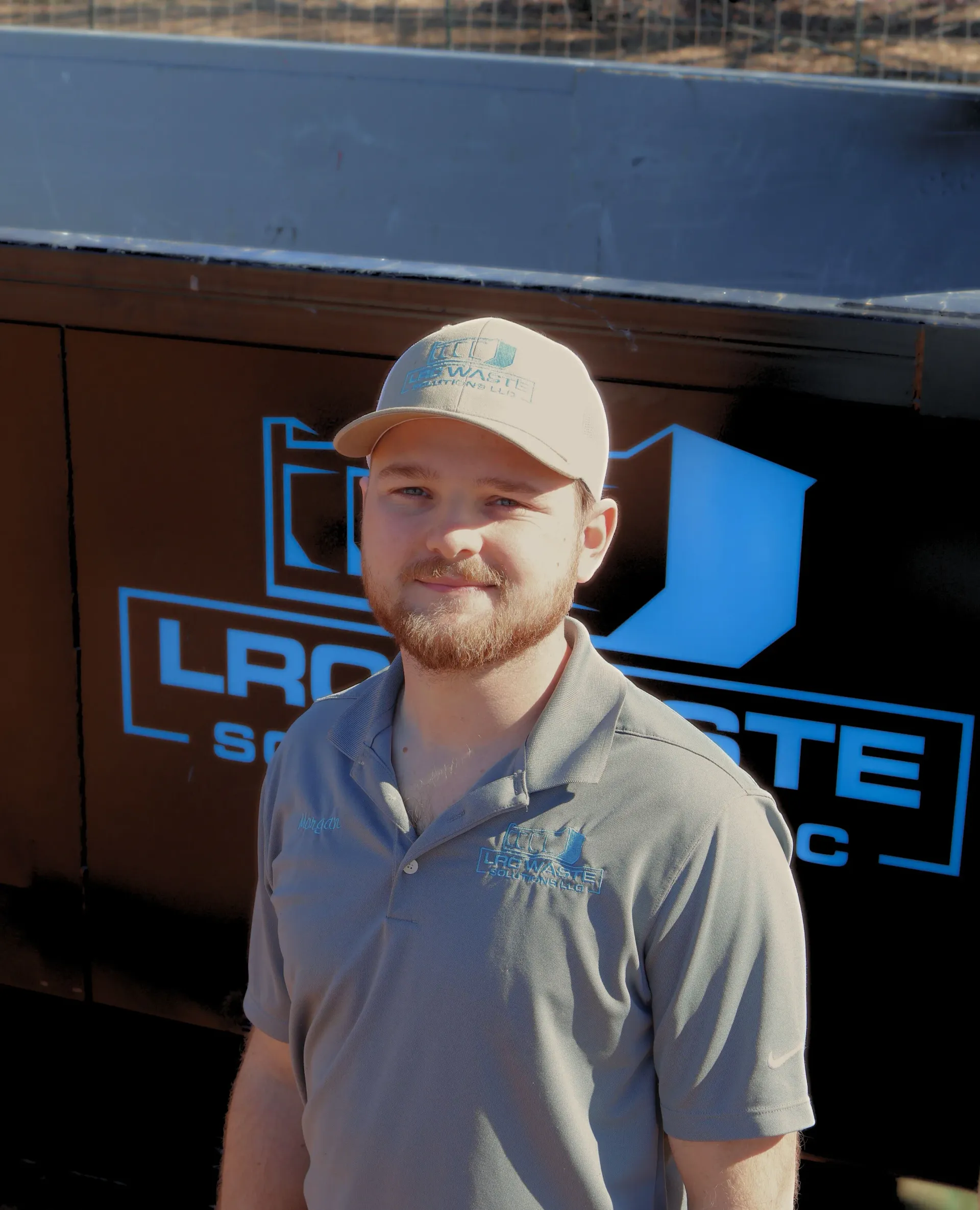 A man wearing a hat is standing in front of a dumpster that says lrc