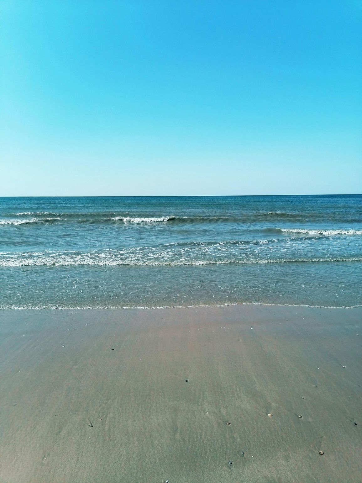Calm ocean waves meeting a sandy beach under a bright blue sky