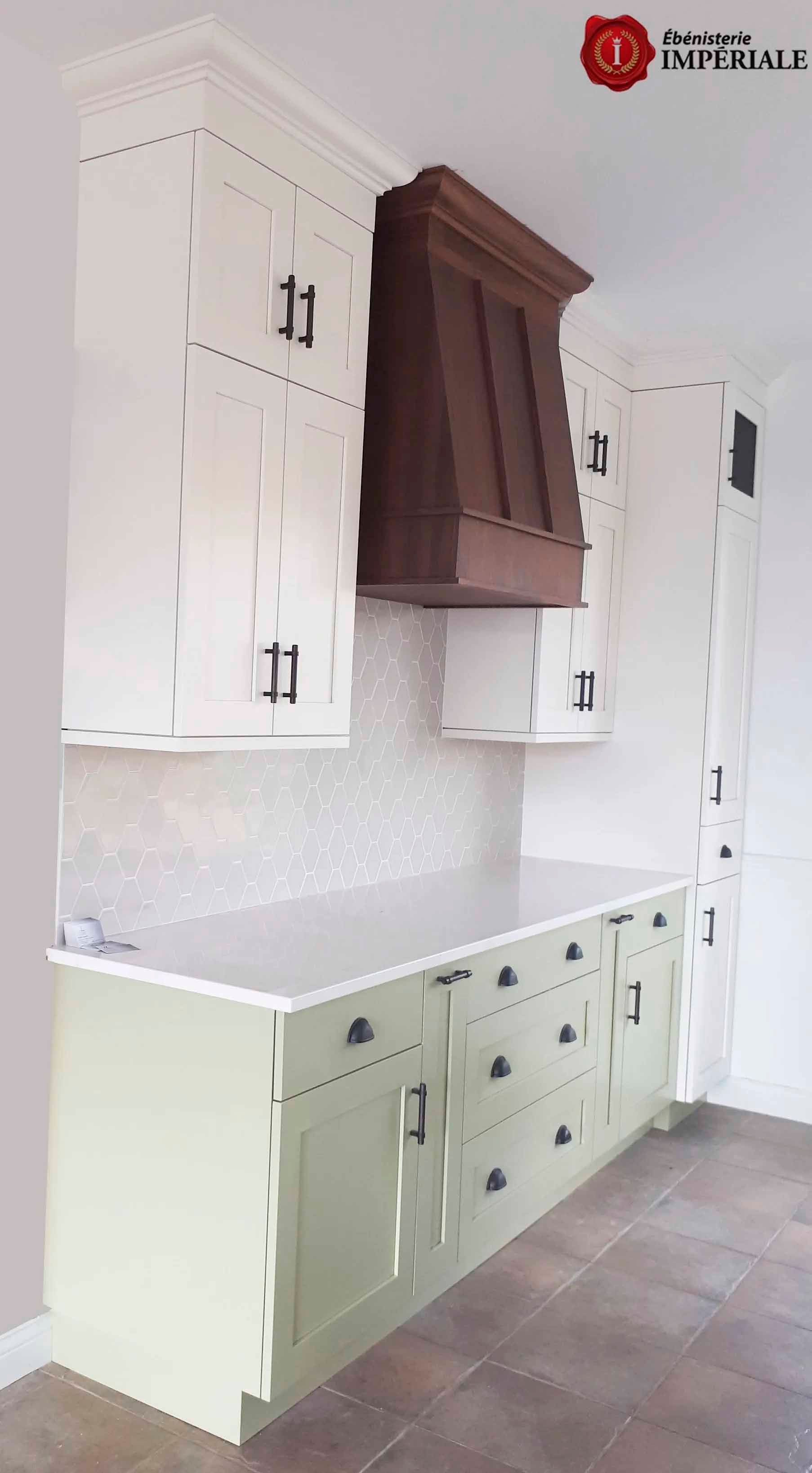 Armoires de cuisine peintes en blanc et vert, hotte aspirante marron, comptoir blanc et quincaillerie noire.