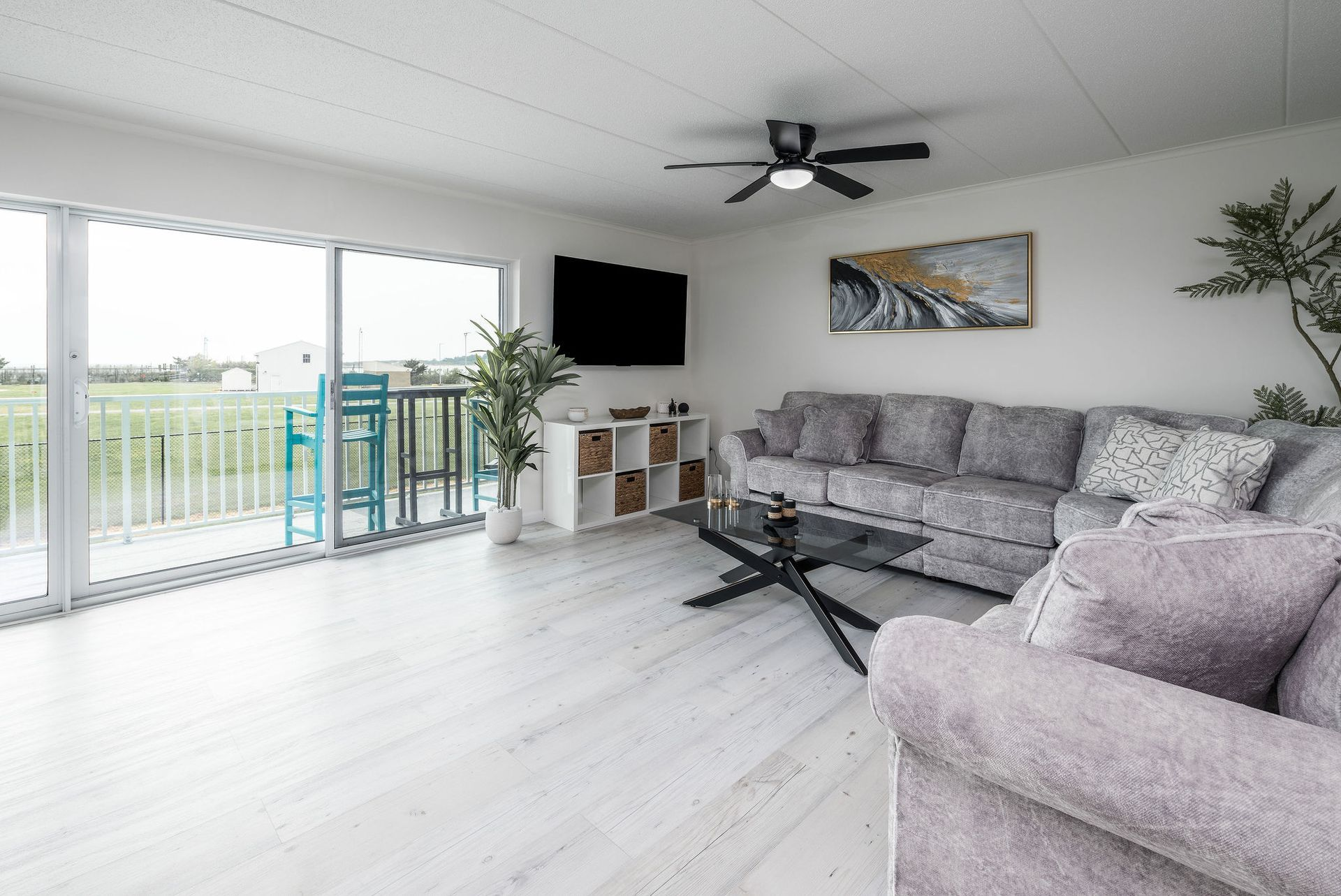 Spacious living room with gray sectional, TV, and sliding glass door overlooking a field.