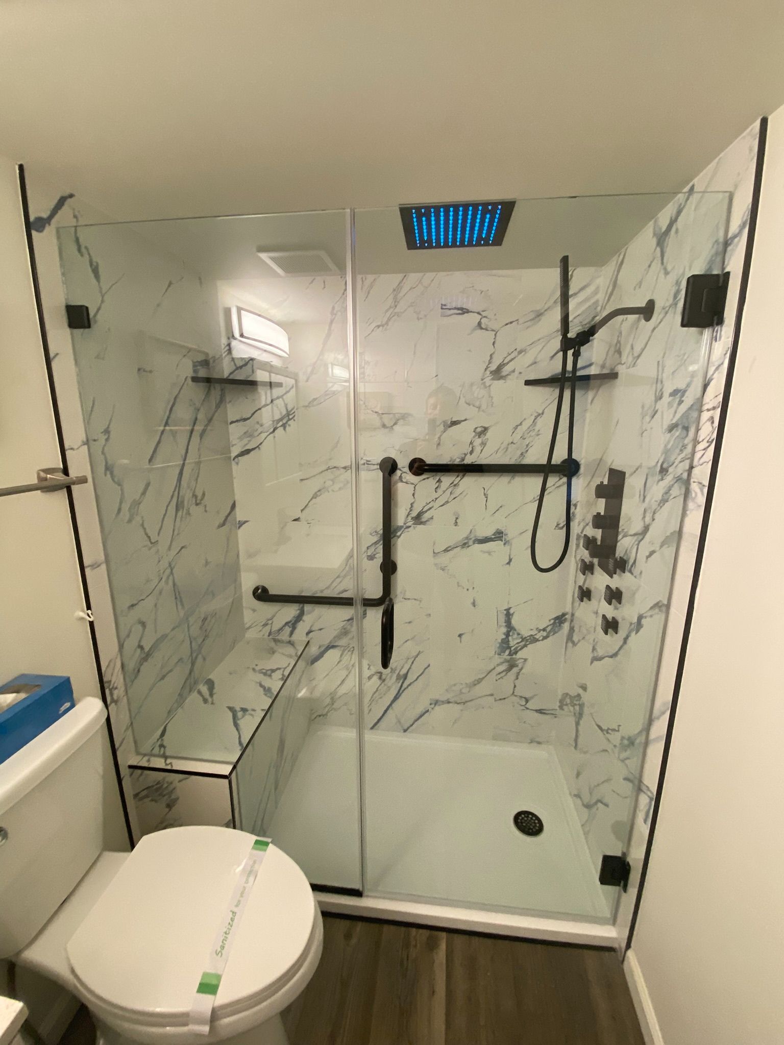 Modern bathroom with glass shower, marble tile, black fixtures, grab bars, and toilet.