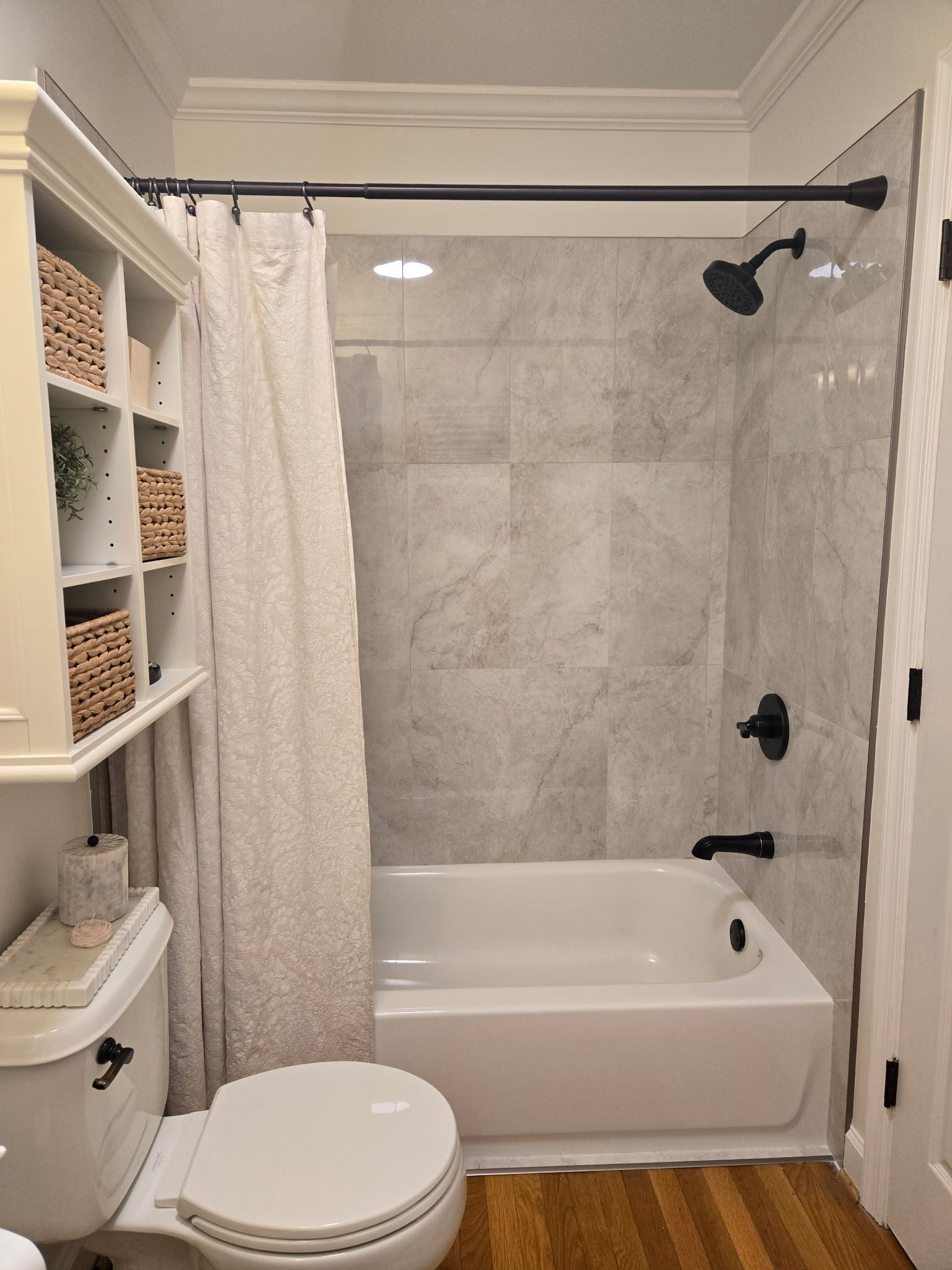 Bathroom with white tub, gray tiled shower, toilet, and a cabinet with wicker baskets.