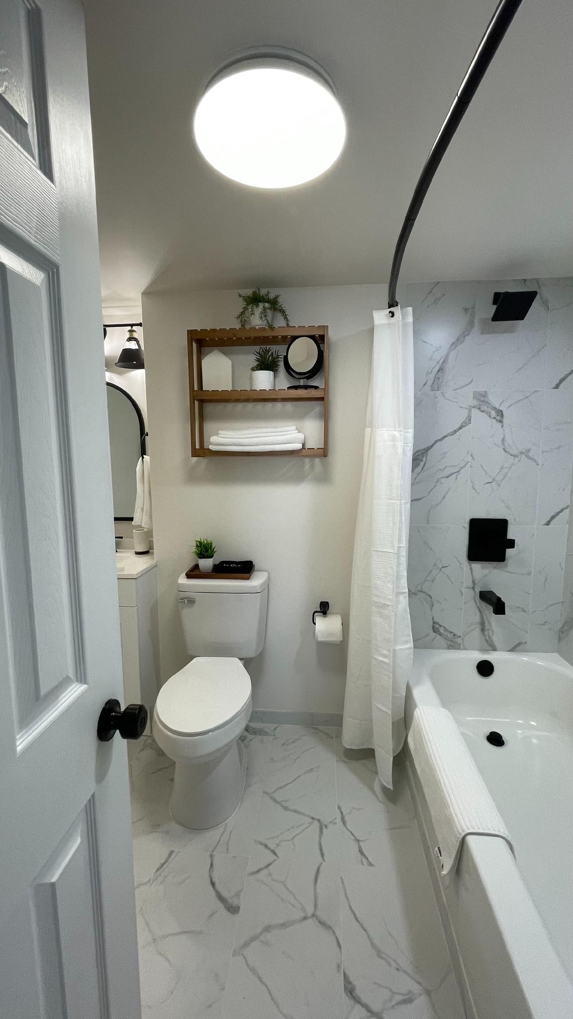 Bathroom with a white marble-look floor and walls, a white tub, and a round overhead light.
