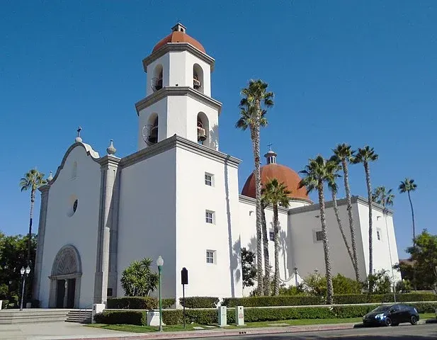 a white church with a bell tower and palm trees in front of it