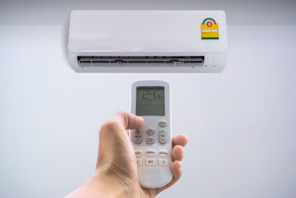A Person Is Holding A Remote Control In Front Of An Air Conditioner — Mackies In Lake Cathie, NSW