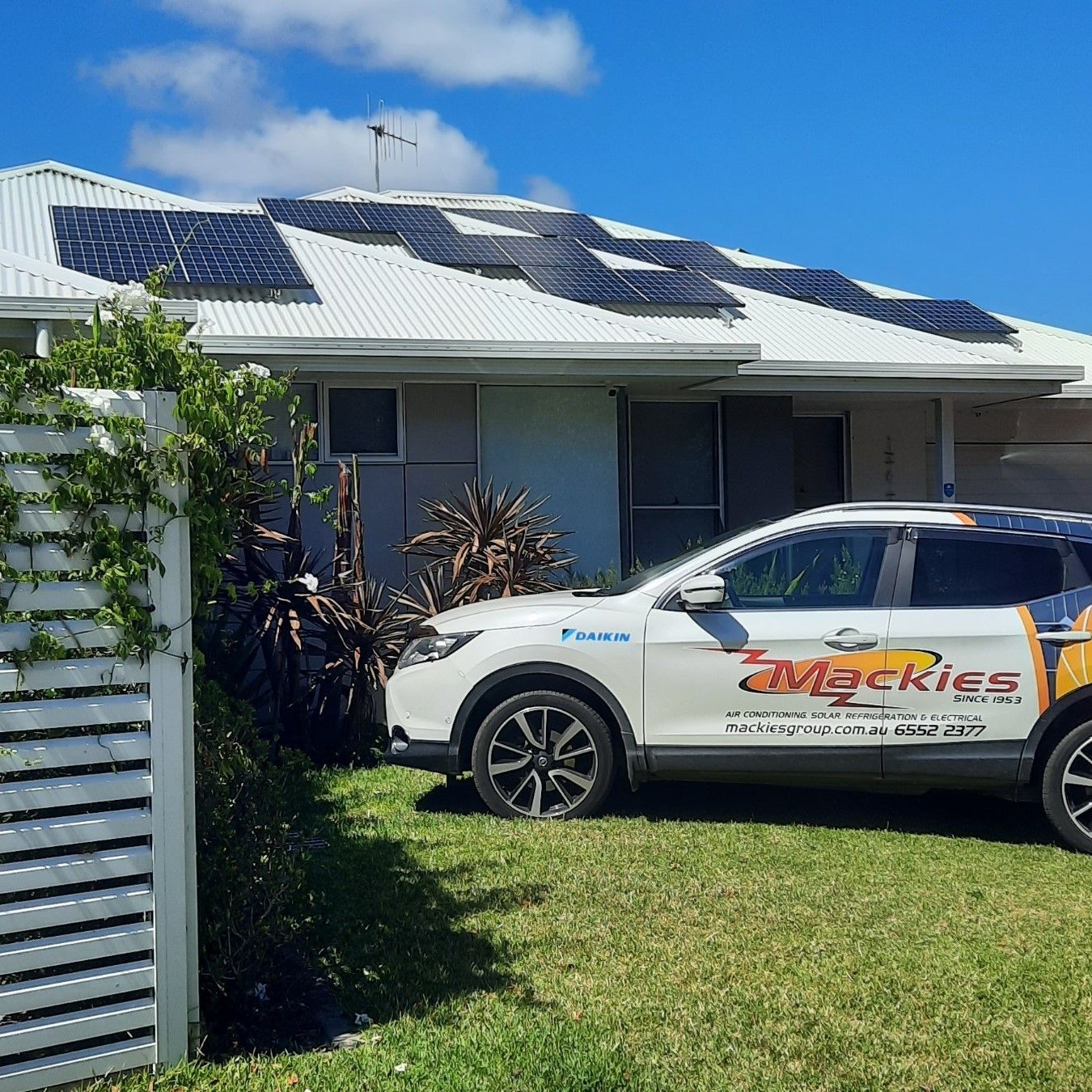 A White Car Is Parked In Front Of A House With Solar Panels On The Roof — Mackies In Taree, NSW