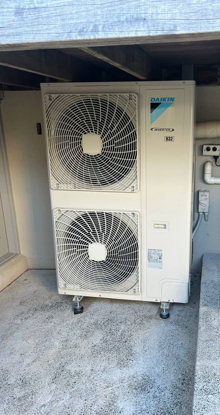 A Large White Air Conditioner Is Sitting Under A Roof — Mackies In Taree, NSW