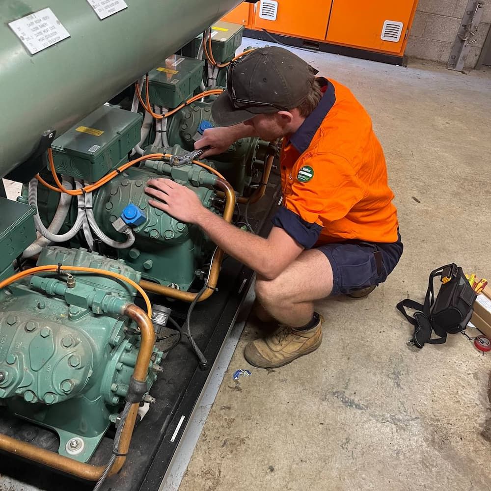 A Man In An Orange Shirt Is Working On A Machine — Mackies In Taree, NSW