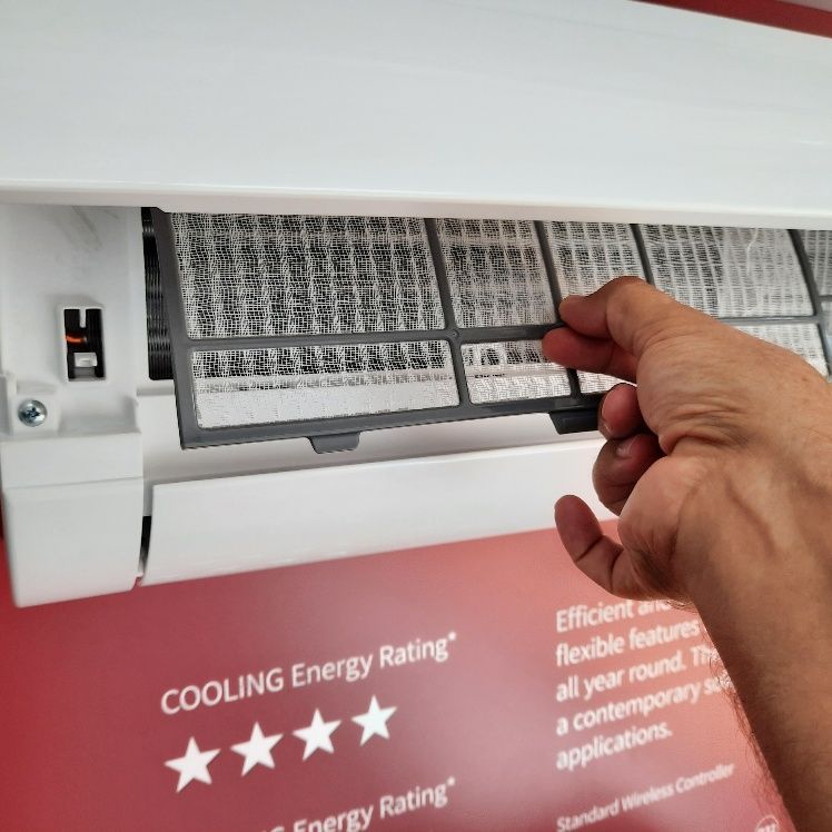 A Person Is Cleaning A Filter On An Air Conditioner — Mackies In Taree, NSW