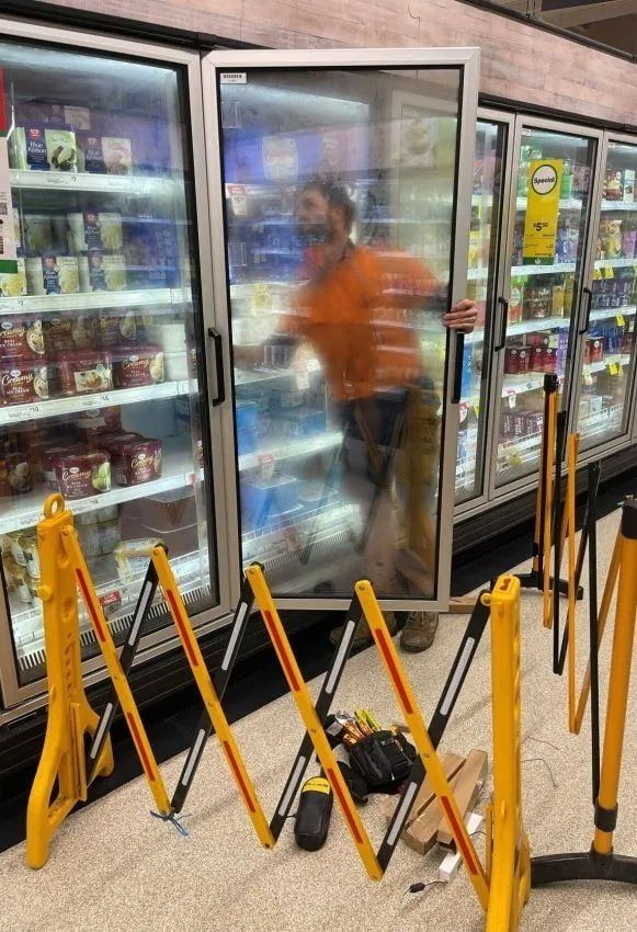 A Man Is Standing In Front Of A Refrigerator In A Store — Mackies In Taree, NSW