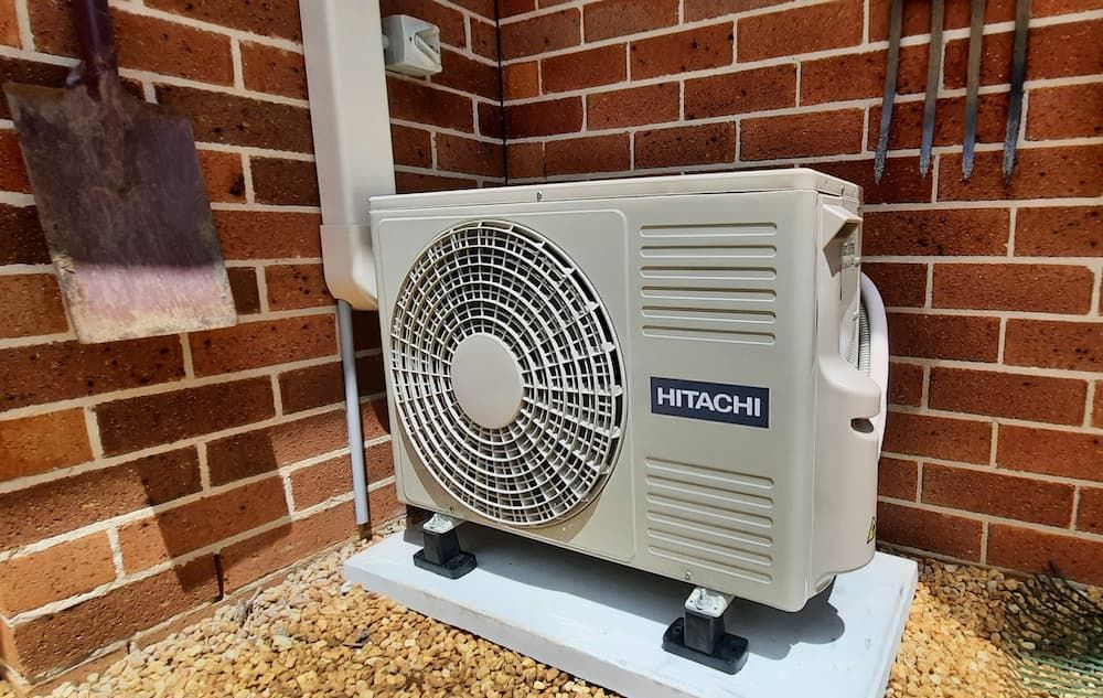 Outdoor Hitachi Air Conditioning Unit Installed Against a Red Brick Wall, Surrounded by Gravel