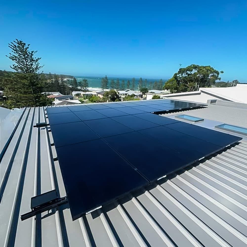 Rooftop Solar Panels on a Metal Roof Overlook a Coastal Neighborhood With Trees and a Clear Blue Sky
