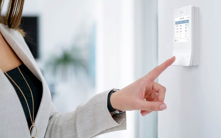 Person adjusting a wall-mounted digital thermostat in a modern home