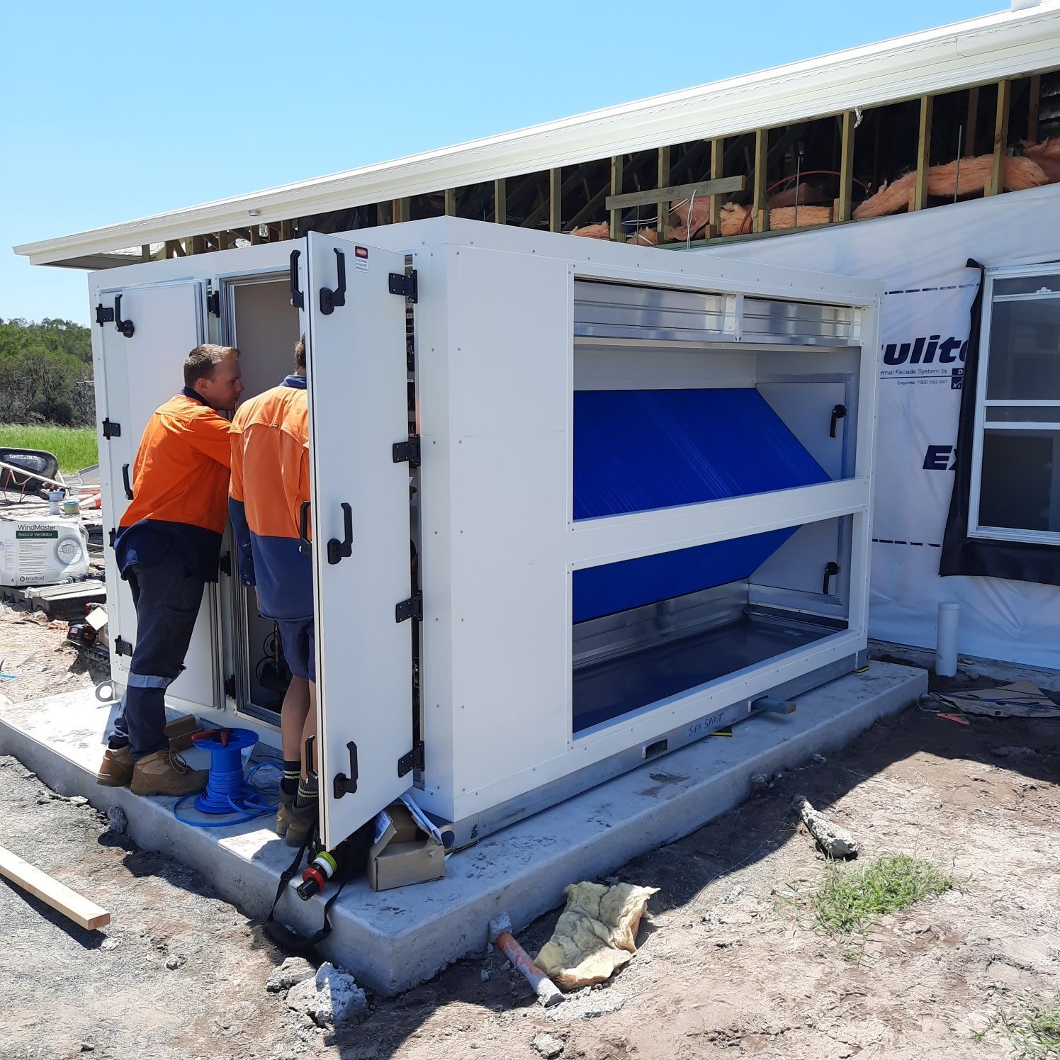 Two Construction Workers Installing A Large White Machinery — Mackies in Taree, NSW