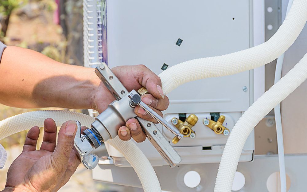 A Man Is Working On An Air Conditioner With A Hose Attached To It — Mackies In Wingham, NSW