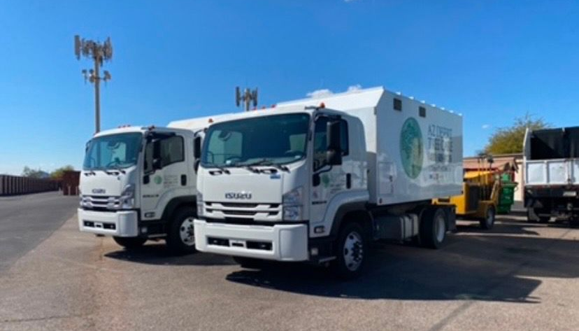 Two white Isuzu trucks parked outside on a sunny day. One has a white storage container.