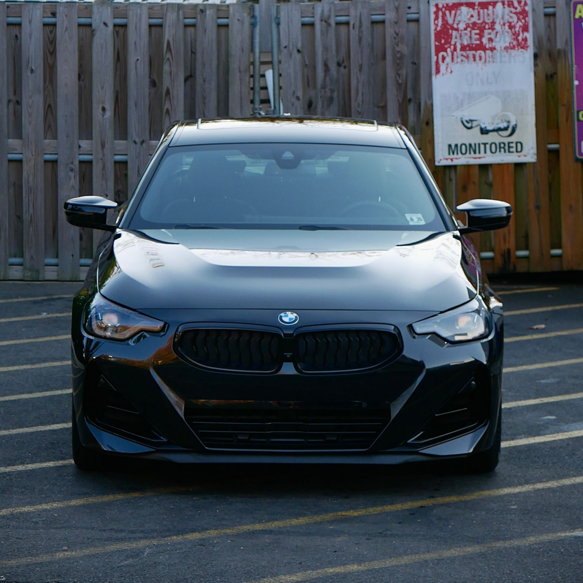 Black BMW car parked in front of a wooden fence.