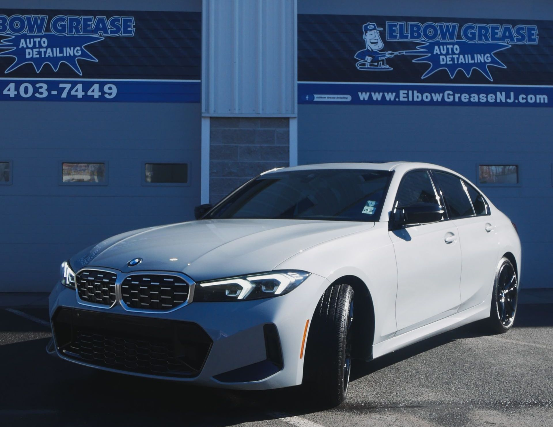 White BMW sedan parked in front of an auto detailing shop with a blue and white sign.
