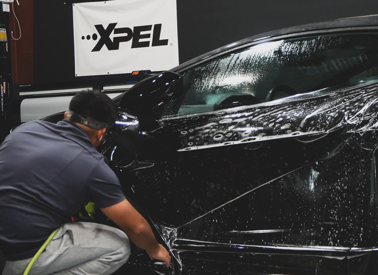 Technician washing a black car in an XPEL detailing bay
