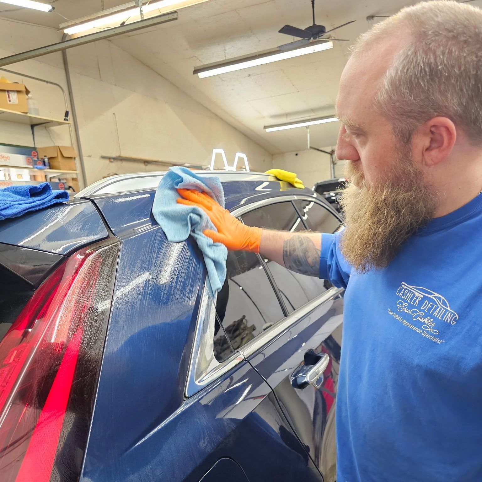 A man with a beard is cleaning a car with a cloth.