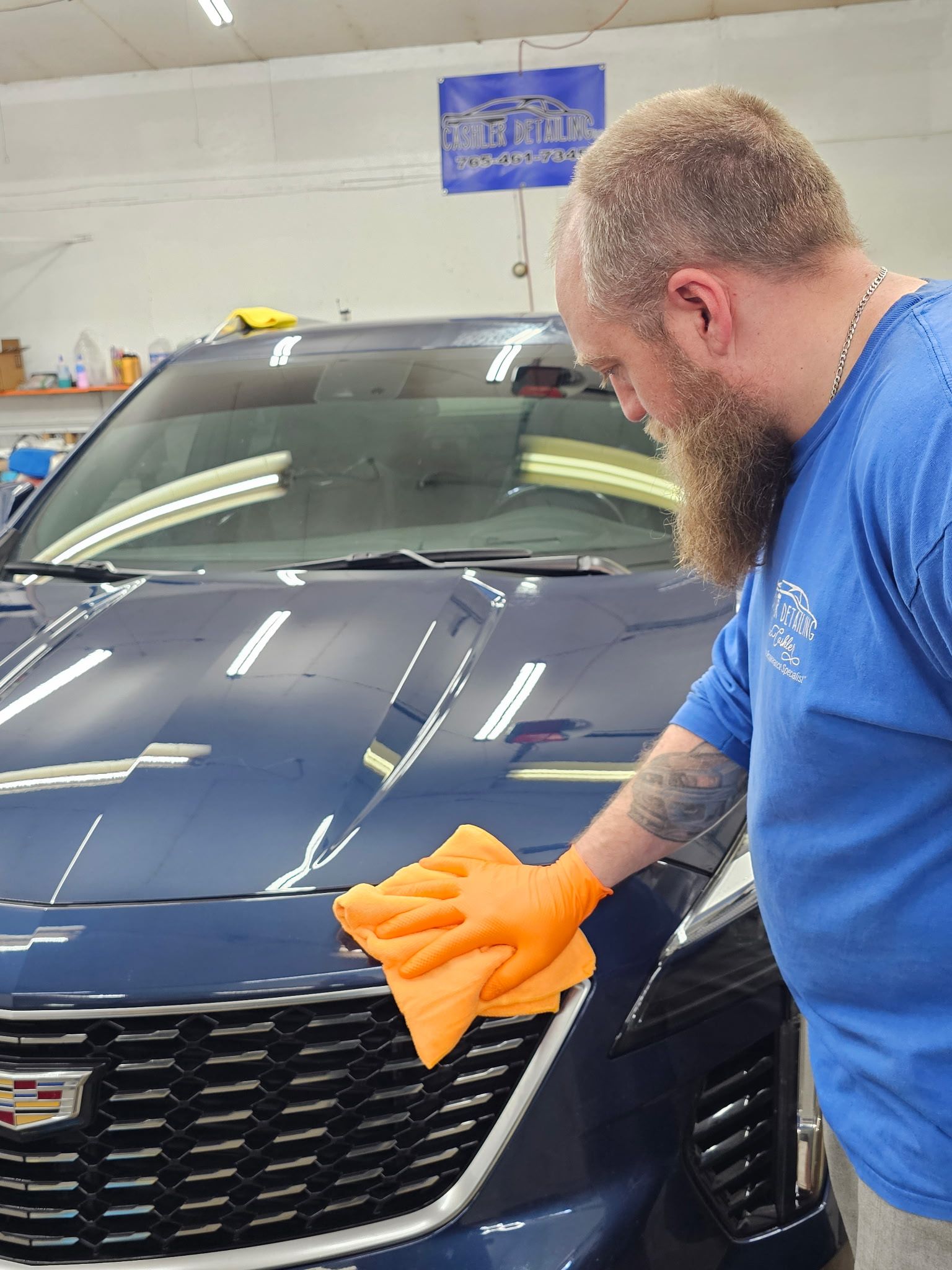 A man is cleaning the hood of a car with an orange cloth.