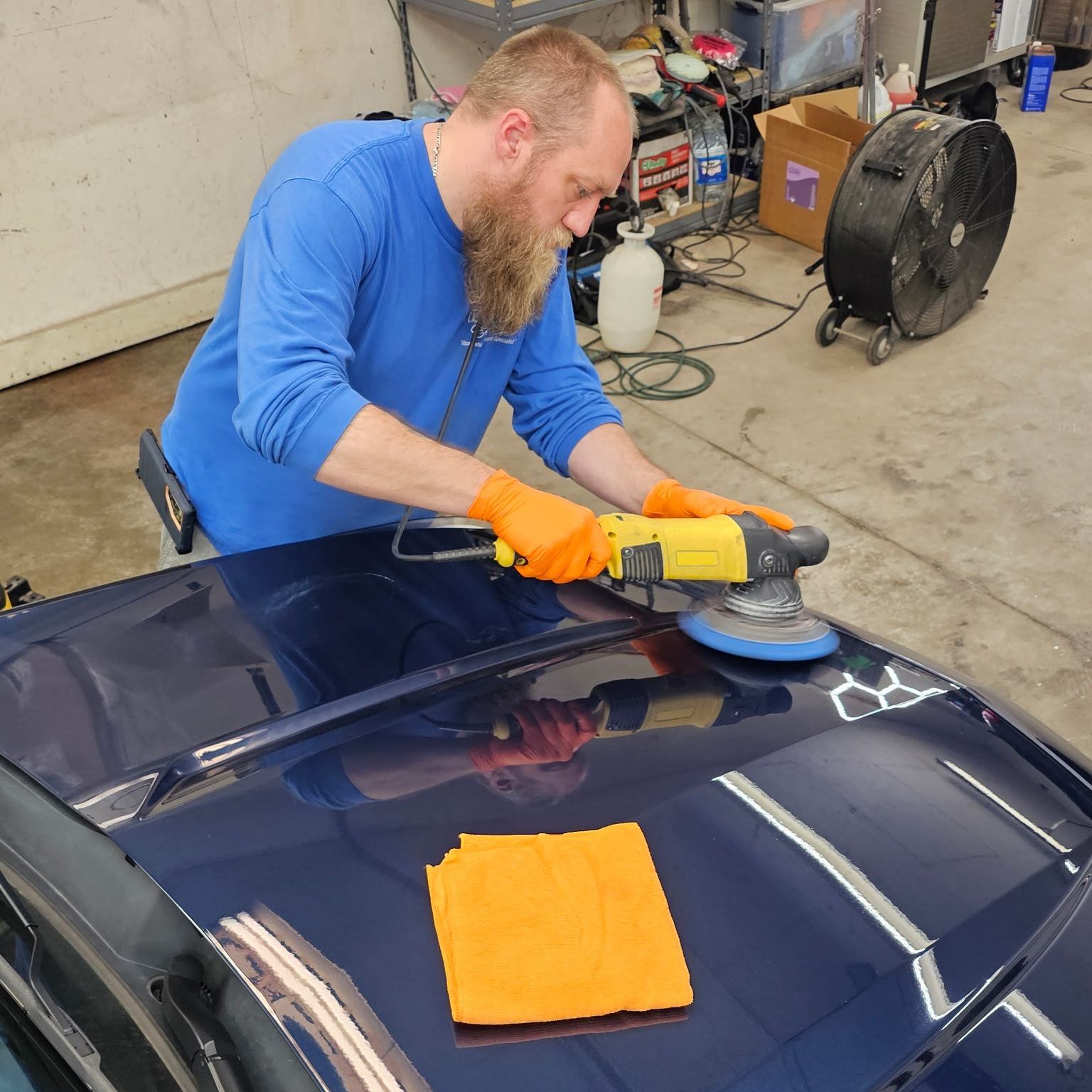 A man is polishing the hood of a car in a garage.