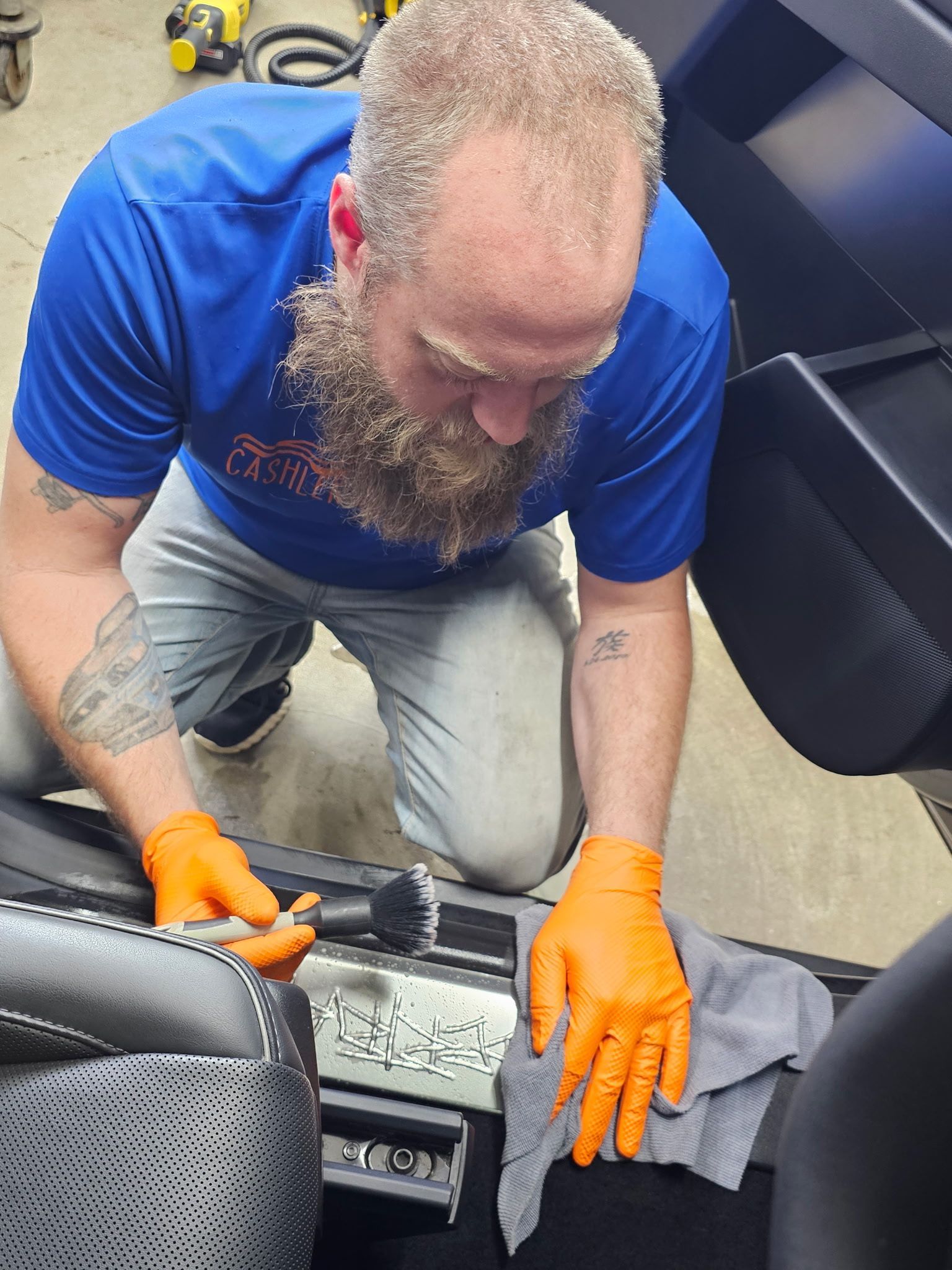 A man with a beard wearing orange gloves is cleaning a car seat.