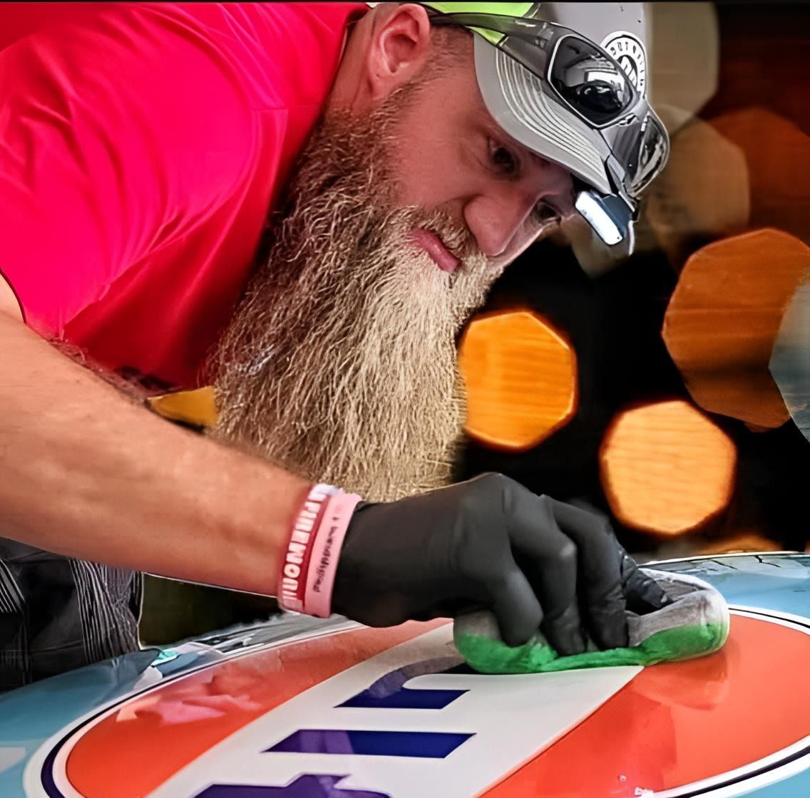 A man with a beard wearing a red shirt is cleaning a sign with a sponge