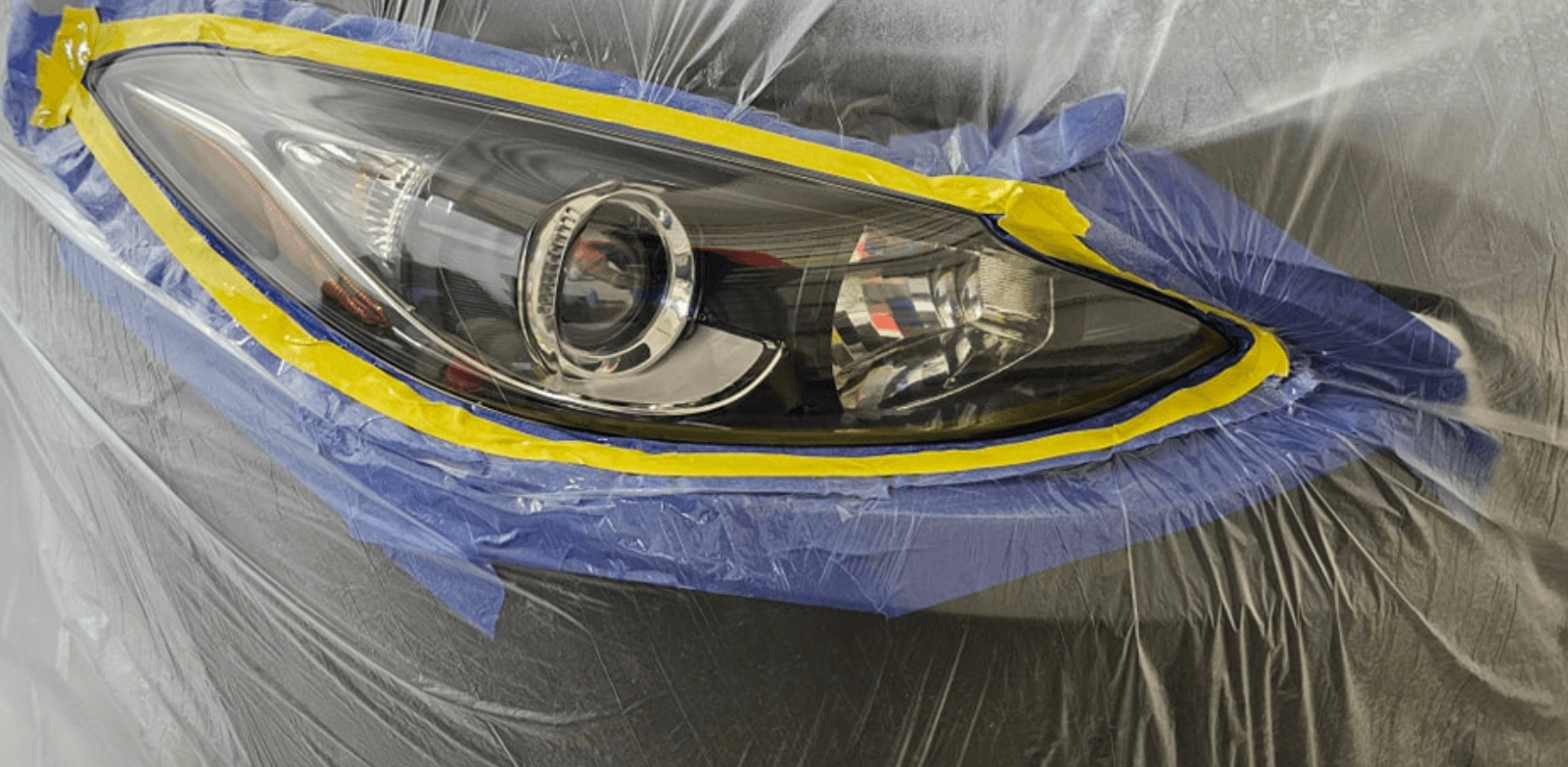 A car headlight is wrapped in plastic wrap and tape.