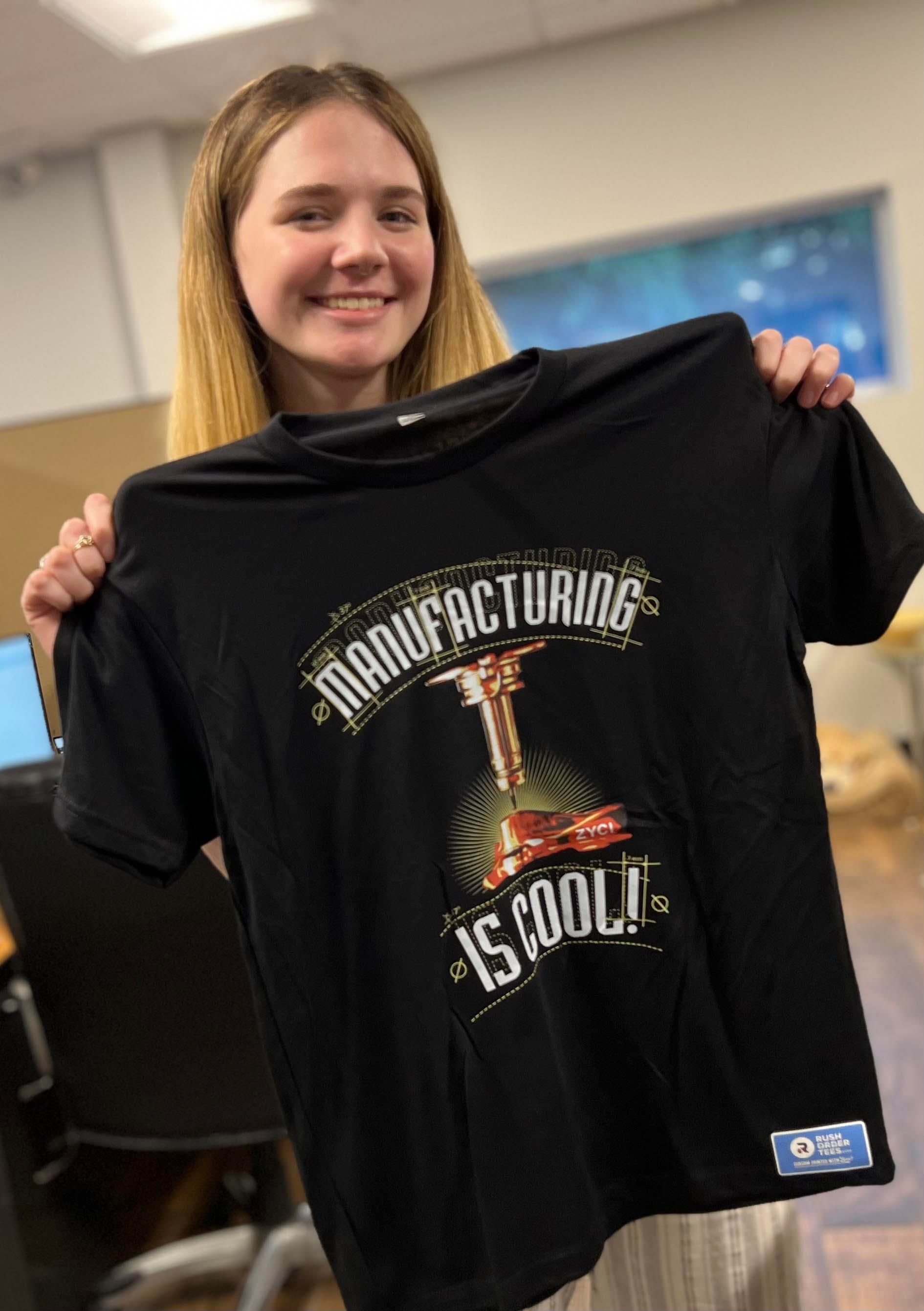 A woman is holding a black t-shirt that says `` manufacturing is cool ''.