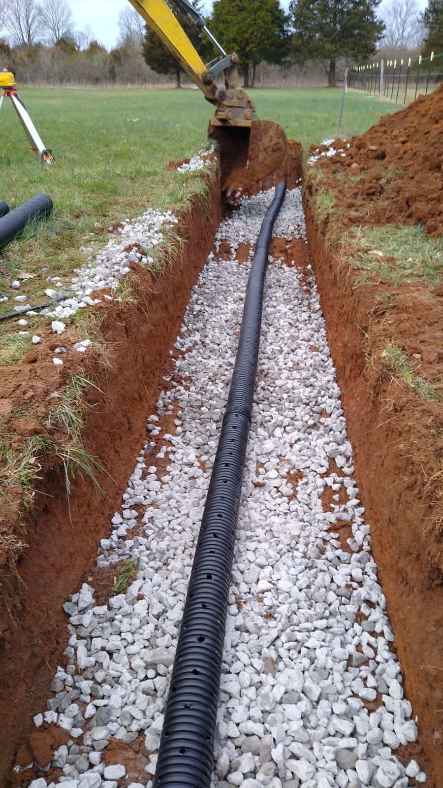 A black pipe is being installed in a trench filled with gravel.