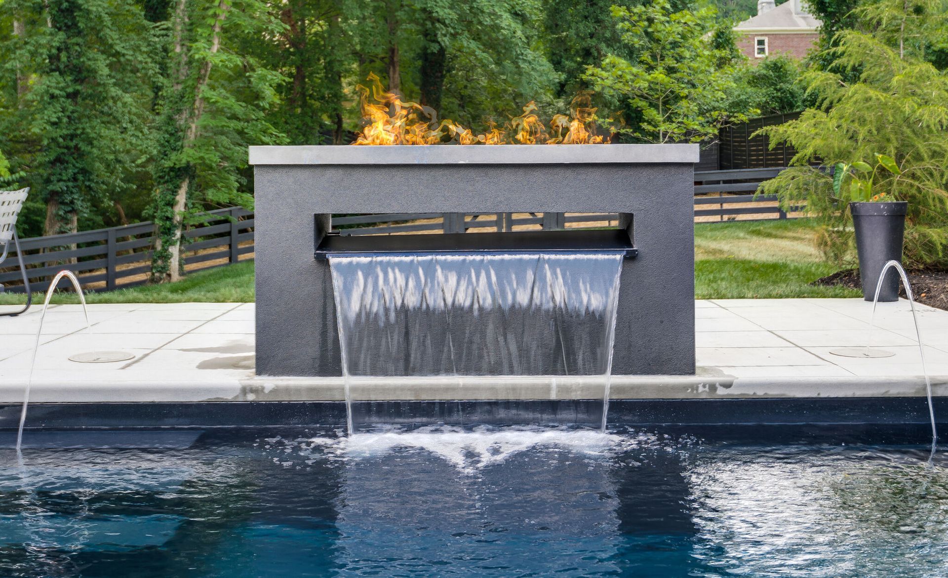 A swimming pool with a waterfall and a fire pit in the background.